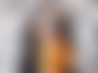 A dog in a black cape holds a pumpkin in their mouth.