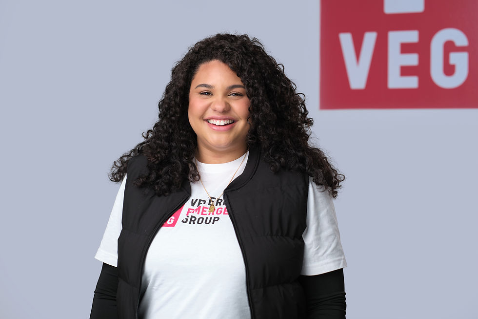 Smiling woman with long dark curly hair wearing a white shirt that says Veterinary Emergency Group and a black vest. 