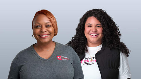 Two smiling women smiling with a gray background behind them.