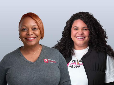 Two smiling women smiling with a gray background behind them.