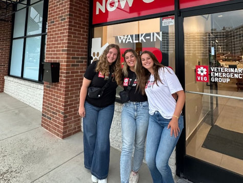 Three women stading in front of a VEG ER for Pets hospital, wearing VEG t-shirts and smiling.