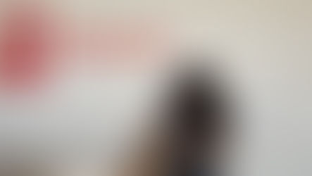 A black dog is sitting and being pet by a veterinary staff member wearing scrubs.