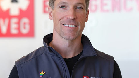 A man smiling at the camera wearing a vest with a black t-shirt underneath.