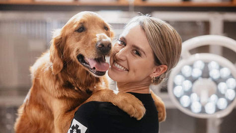 A retriever dog is held by a smiling veterinarian