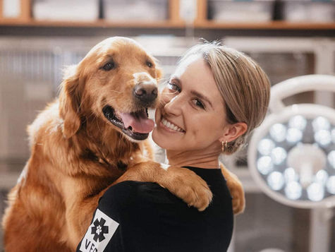 A retriever dog is held by a smiling veterinarian