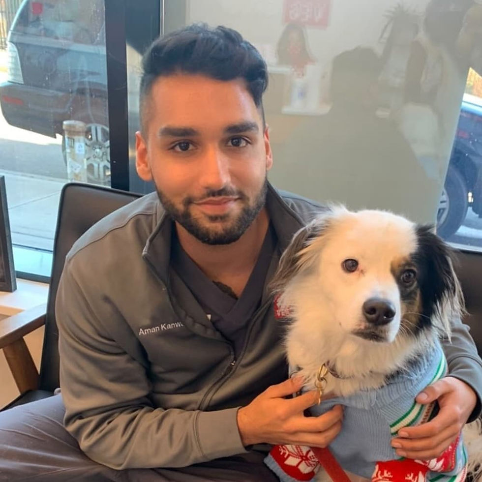 A veterinarian at VEG sits in a chair in the animal hospital and smiles at the camera while hugging a white and black dog.