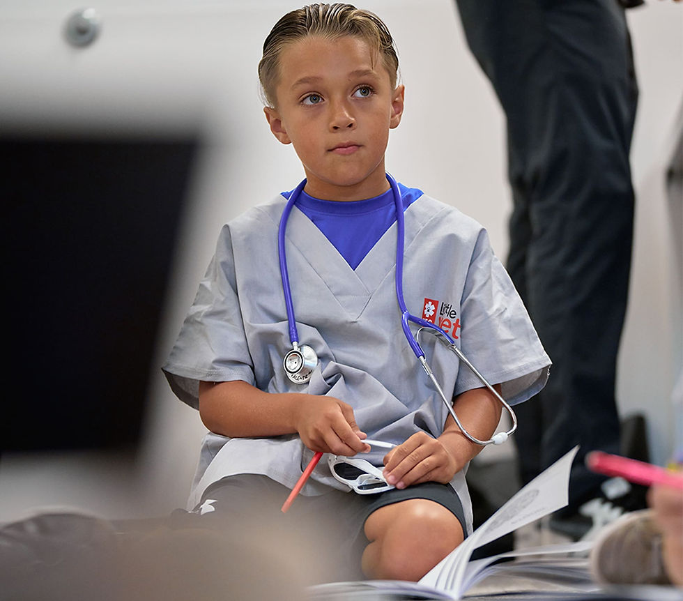 A little boy wearing scrubs and a stethoscope listens to a veterinarian