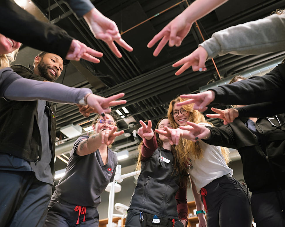 A group of doctors, nurses, and hospital staff standing in a circle making a peace sign with their fingers and arms extended outward