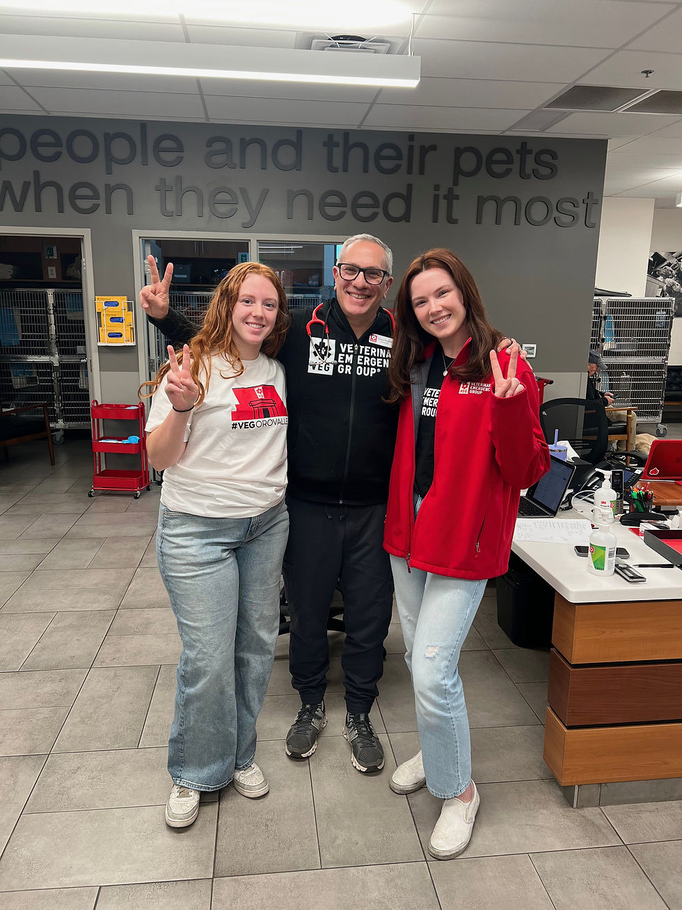 Three people standing together in a veterinary hospital smiling at the camera.